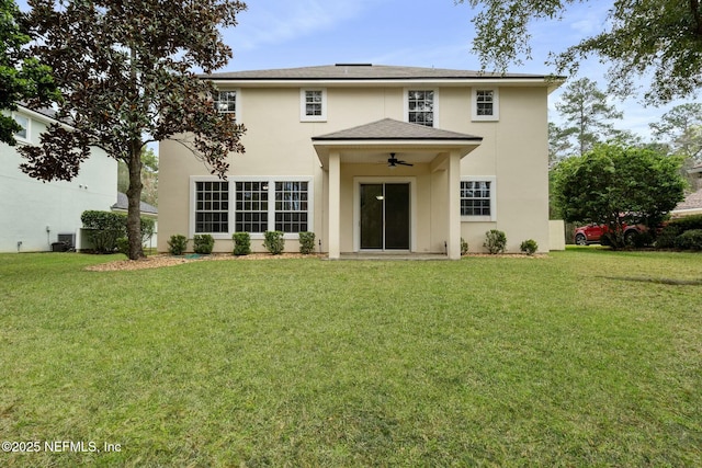 back of property with a ceiling fan, a lawn, and stucco siding