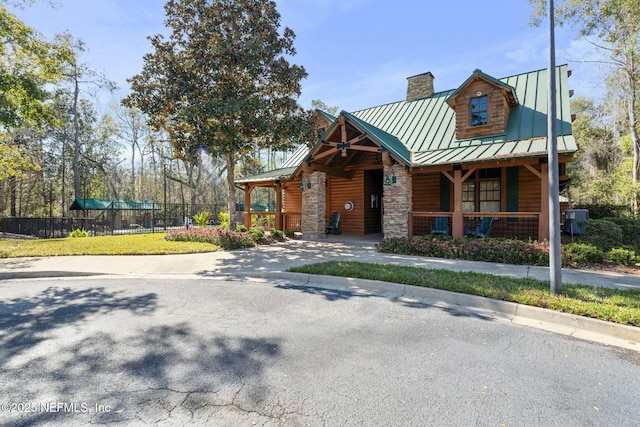 view of front of house featuring stone siding, a chimney, a standing seam roof, fence, and a porch