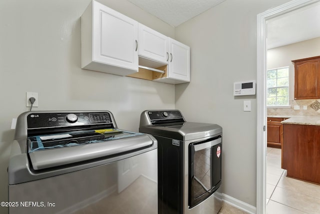 laundry area featuring light tile patterned floors, separate washer and dryer, cabinet space, and baseboards