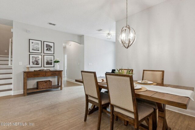 dining area with arched walkways, stairway, light wood-type flooring, and baseboards