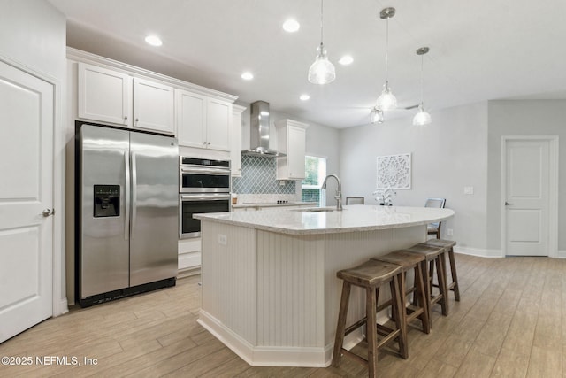 kitchen featuring light wood-style flooring, a sink, stainless steel appliances, wall chimney exhaust hood, and tasteful backsplash