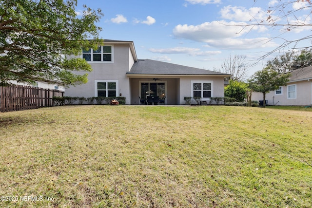 rear view of house with fence, roof with shingles, stucco siding, a lawn, and a ceiling fan