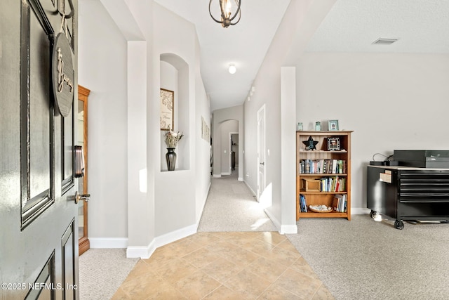 corridor featuring light carpet, visible vents, arched walkways, baseboards, and light tile patterned flooring