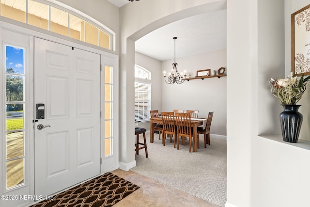 carpeted entrance foyer with arched walkways, baseboards, and an inviting chandelier