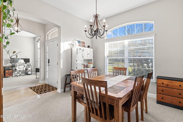 carpeted dining area featuring baseboards, arched walkways, and a notable chandelier