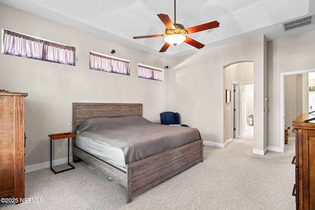 carpeted bedroom featuring arched walkways, ceiling fan, visible vents, and baseboards