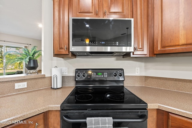 kitchen with brown cabinets, light countertops, black electric range, and stainless steel microwave