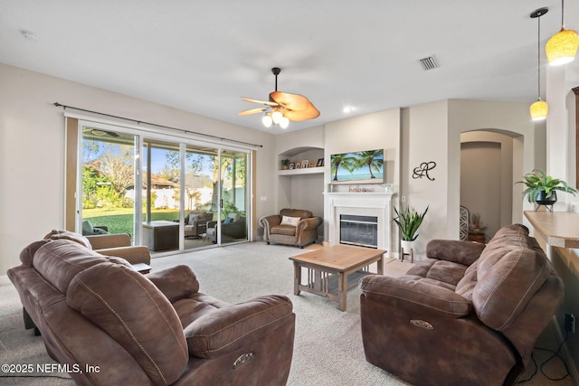 living room featuring visible vents, built in features, arched walkways, a glass covered fireplace, and carpet floors