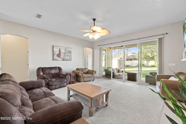 living area featuring a ceiling fan, arched walkways, visible vents, and carpet flooring