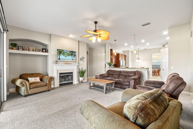 living room featuring built in features, visible vents, a glass covered fireplace, light carpet, and baseboards