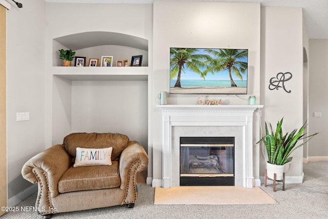 sitting room with a fireplace with flush hearth, carpet, baseboards, and built in shelves