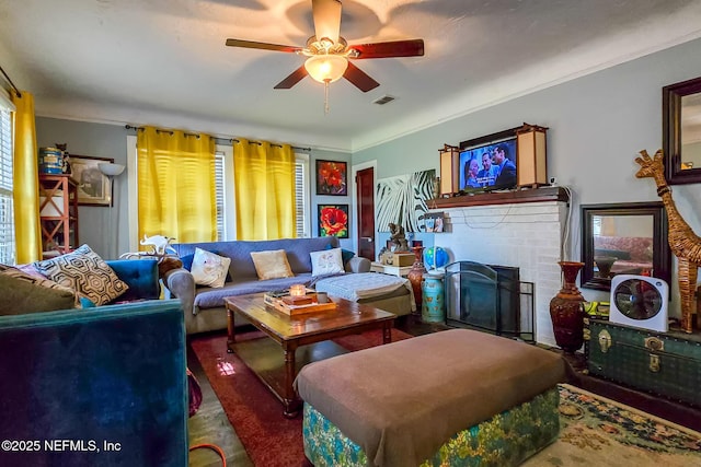 living room with a brick fireplace, ceiling fan, visible vents, and crown molding