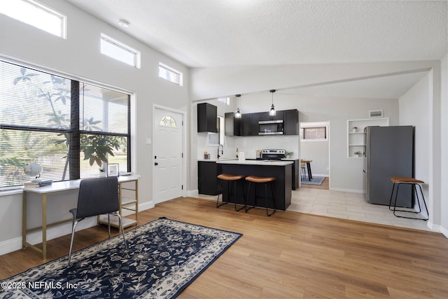 kitchen featuring light wood finished floors, light countertops, appliances with stainless steel finishes, dark cabinetry, and a peninsula