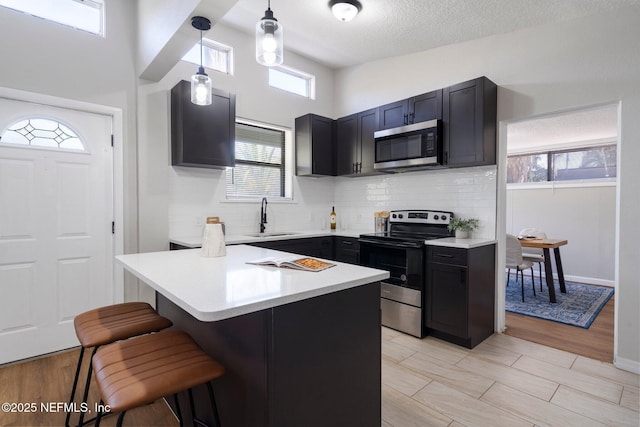 kitchen featuring a breakfast bar area, stainless steel appliances, a sink, light countertops, and tasteful backsplash