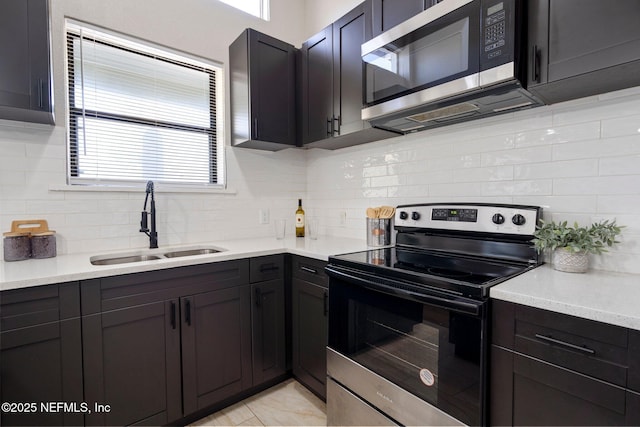 kitchen featuring appliances with stainless steel finishes, light countertops, a sink, and decorative backsplash