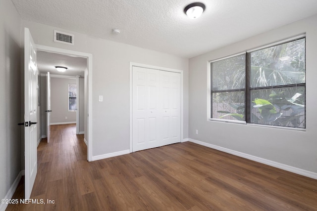 unfurnished bedroom with a closet, visible vents, a textured ceiling, wood finished floors, and baseboards