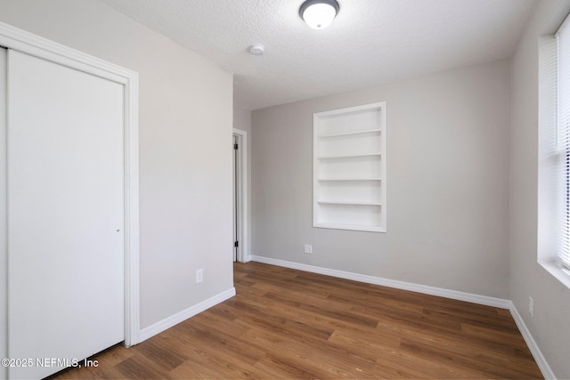 unfurnished bedroom with a closet, a textured ceiling, baseboards, and wood finished floors