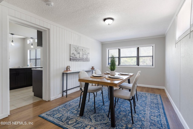 dining area with light wood-type flooring, baseboards, ornamental molding, and a textured ceiling