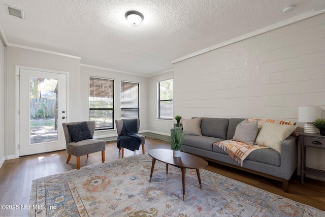 living area with baseboards, visible vents, ornamental molding, wood finished floors, and a textured ceiling