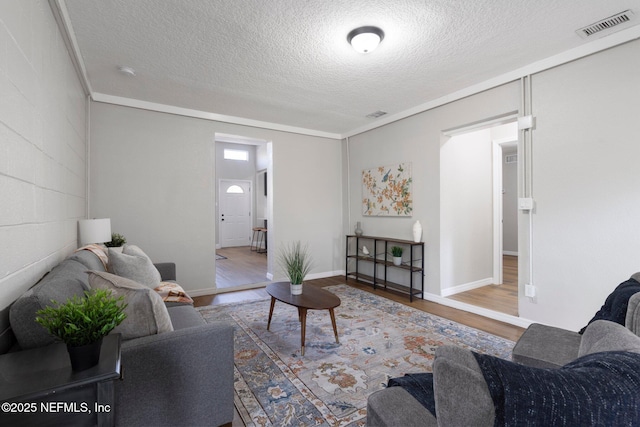 living room featuring a textured ceiling, wood finished floors, visible vents, baseboards, and concrete block wall