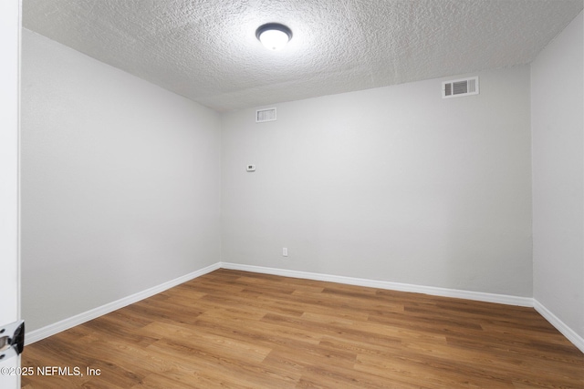 spare room featuring a textured ceiling, light wood finished floors, visible vents, and baseboards