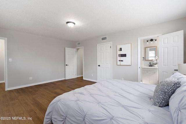 bedroom with a textured ceiling, connected bathroom, wood finished floors, visible vents, and baseboards