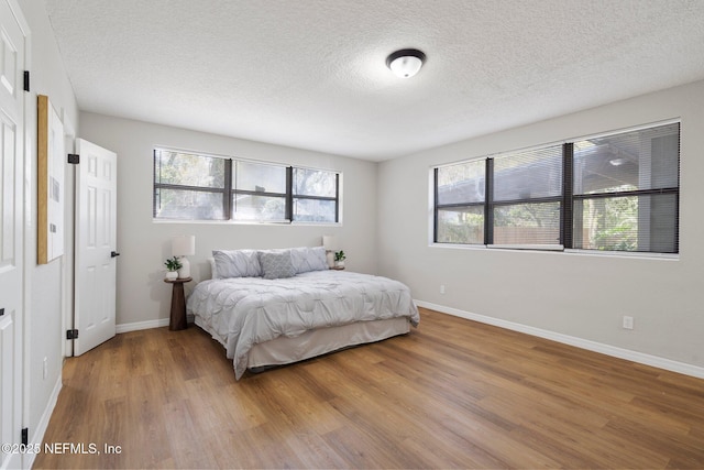 bedroom with a textured ceiling, baseboards, and wood finished floors