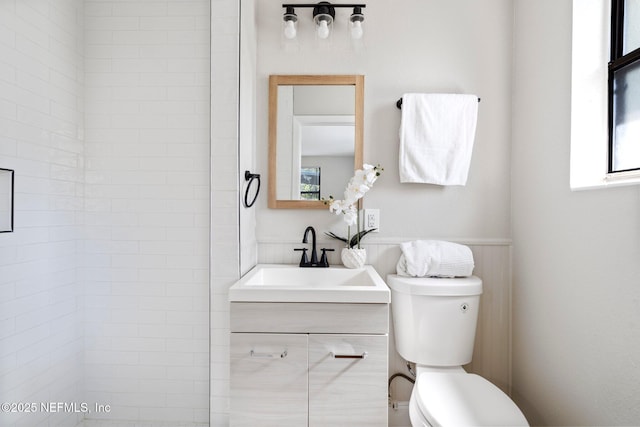 bathroom featuring a tile shower, vanity, and toilet