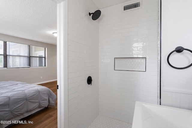 full bath with a textured ceiling, tiled shower, wood finished floors, and visible vents