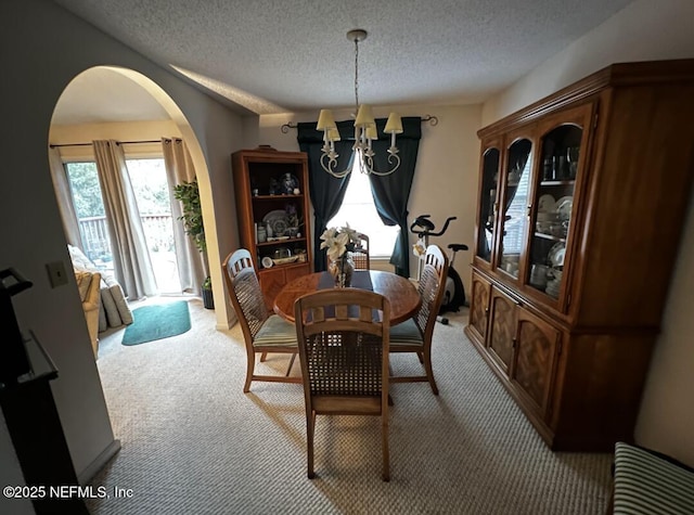 dining room featuring arched walkways, light colored carpet, a textured ceiling, and an inviting chandelier