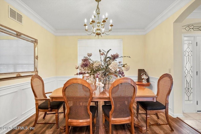 dining area with a wainscoted wall, a textured ceiling, wood finished floors, and visible vents