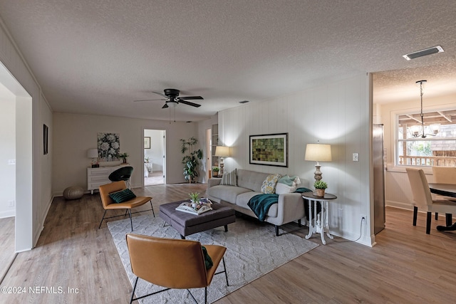 living area with a textured ceiling, ceiling fan with notable chandelier, wood finished floors, and visible vents