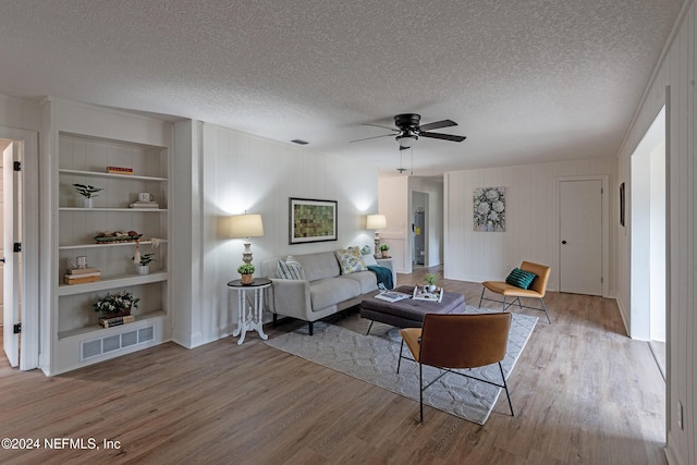 living room with visible vents, a textured ceiling, built in features, and wood finished floors