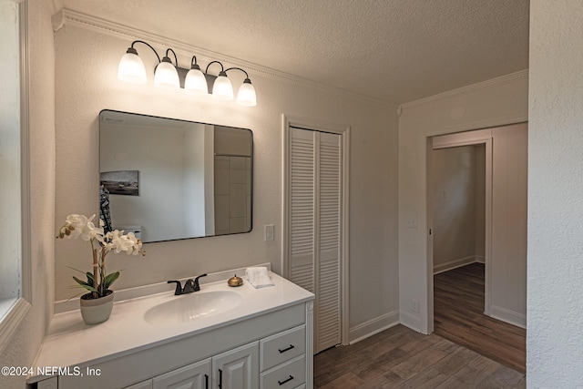 bathroom featuring a textured ceiling, wood finished floors, vanity, baseboards, and crown molding