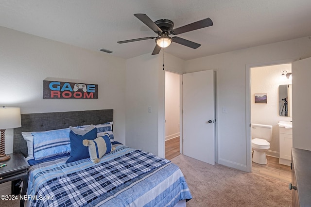 bedroom with light carpet, baseboards, visible vents, a ceiling fan, and ensuite bathroom