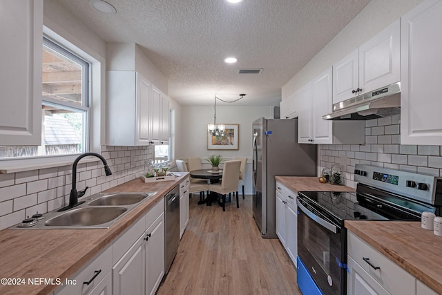 kitchen with under cabinet range hood, stainless steel appliances, a sink, white cabinets, and wooden counters