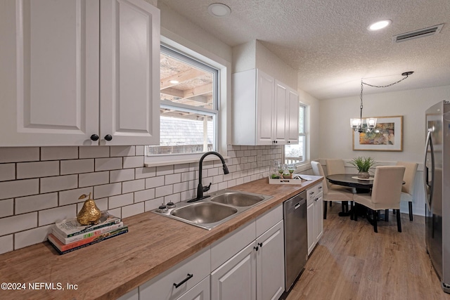 kitchen with stainless steel appliances, visible vents, wooden counters, white cabinetry, and a sink