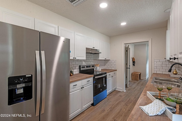 kitchen featuring white cabinets, appliances with stainless steel finishes, under cabinet range hood, wooden counters, and a sink