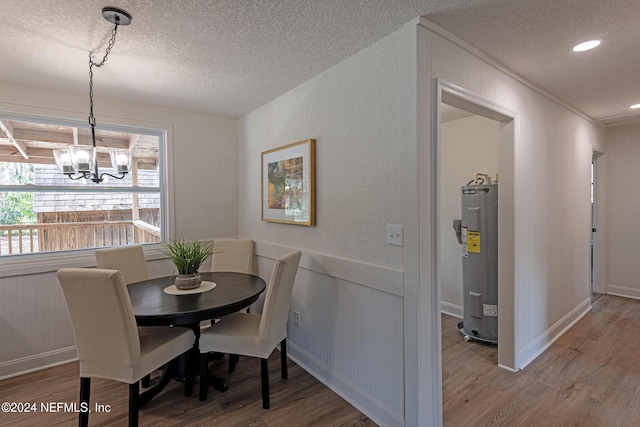 dining area with wainscoting, electric water heater, a textured ceiling, wood finished floors, and a chandelier