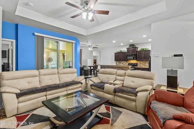 living area with recessed lighting, a raised ceiling, and ceiling fan