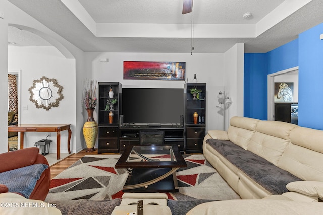 living area featuring a textured ceiling, ceiling fan, a tray ceiling, and wood finished floors