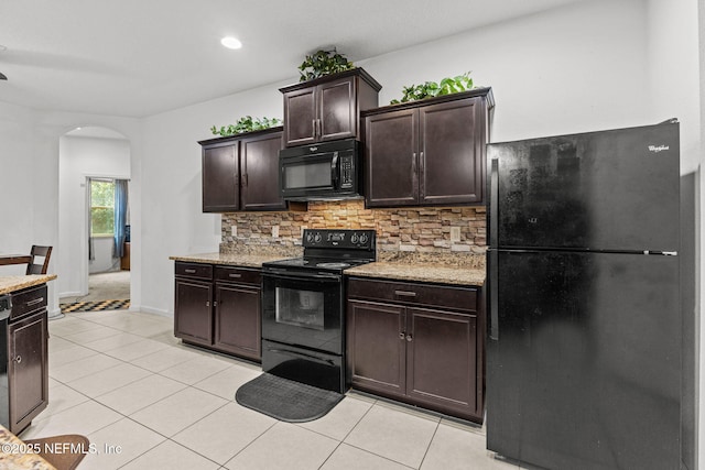 kitchen featuring light tile patterned floors, arched walkways, decorative backsplash, dark brown cabinets, and black appliances