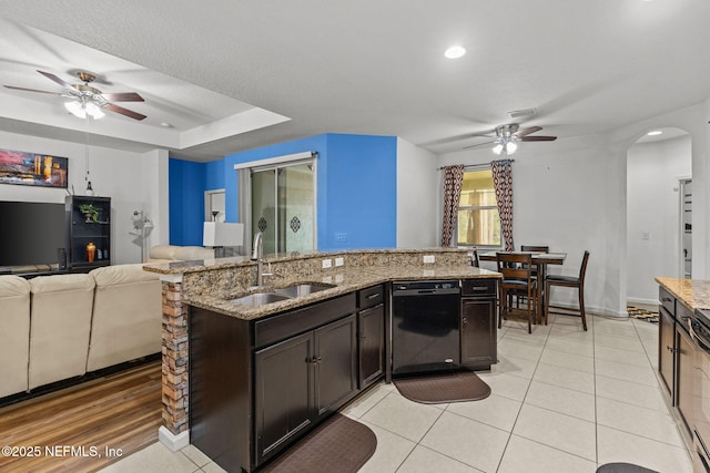 kitchen featuring arched walkways, a sink, open floor plan, light stone countertops, and dishwasher