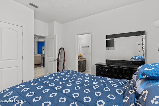 tiled bedroom with visible vents, connected bathroom, and a textured ceiling