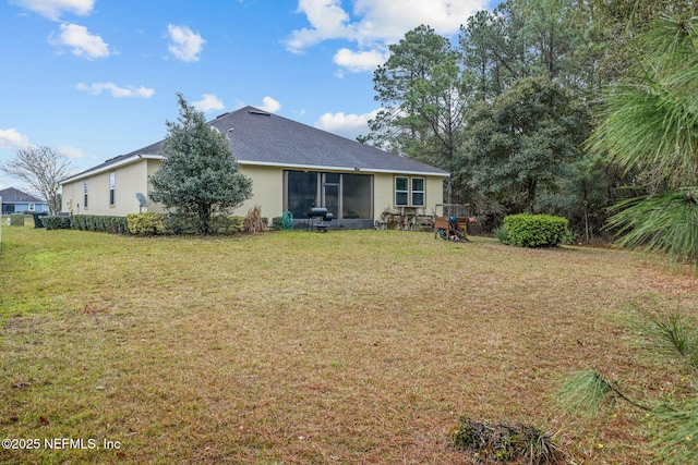 rear view of property featuring a shingled roof, a lawn, and stucco siding