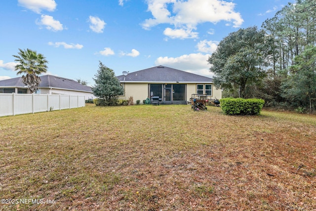 rear view of property featuring a yard, fence, and stucco siding