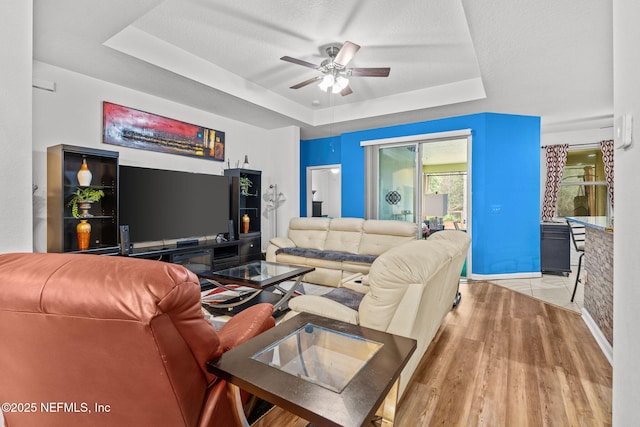 living room featuring a textured ceiling, a ceiling fan, a raised ceiling, and wood finished floors