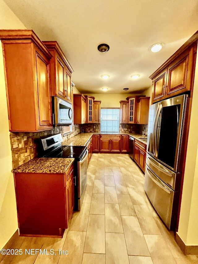 kitchen with brown cabinets, light tile patterned floors, tasteful backsplash, appliances with stainless steel finishes, and glass insert cabinets