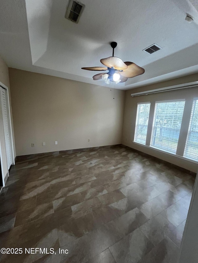 empty room with ceiling fan, visible vents, and baseboards