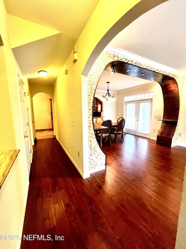 hall featuring baseboards, arched walkways, ornamental molding, wood finished floors, and a notable chandelier